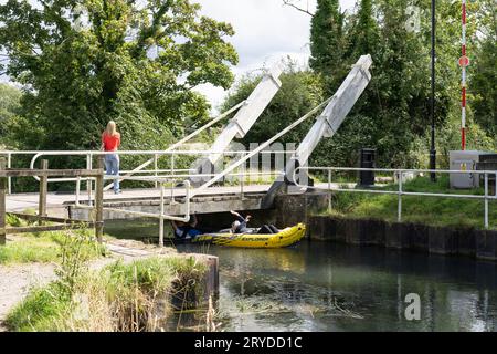 A woman walking over the Warnborough Lift Bridge with a man and woman kayaking passing underneath it on the Basingstoke Canal near Odiham, England Stock Photo