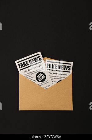 Envelope with FAKE NEWS newspapers over black Stock Photo