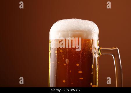 Close up pouring frothy beer in glass over brown Stock Photo