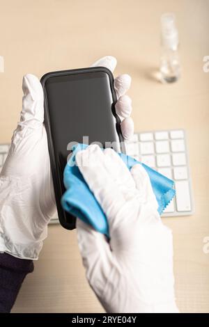 Hands with glove cleaning mobile phone with disinfectant Stock Photo