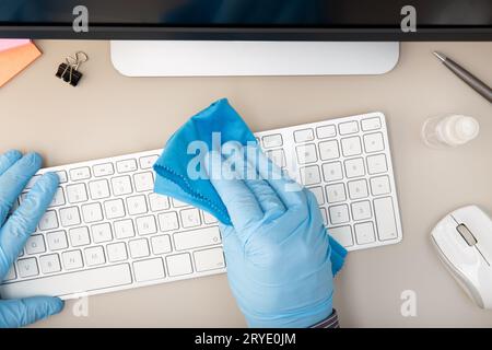 Hand with protective glove cleaning a keyboard with disinfectant Stock Photo