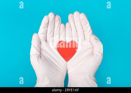 Hands in medical gloves holding a red heart shape model on blue background Stock Photo