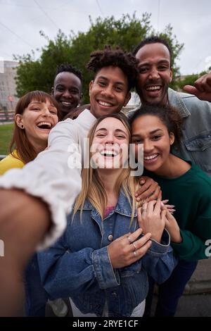 Vertical photo of Cheerful group of friends taking smiling selfie. Group of young people having fun together outdoors at park in the city enjoying Stock Photo