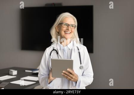 Positive older chief doctor in white coat using tablet computer Stock Photo