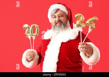 Santa Claus holding balloons in shape of figure 2024 on red background Stock Photo