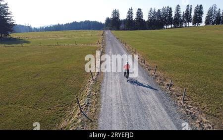 Aerial drone shot of female cyclist on lonely road with shadow Stock Photo