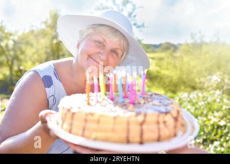 Smiling grandmother holds a birthday homemade cake. Family celebration or a garden party outside in the backyard. Stock Photo