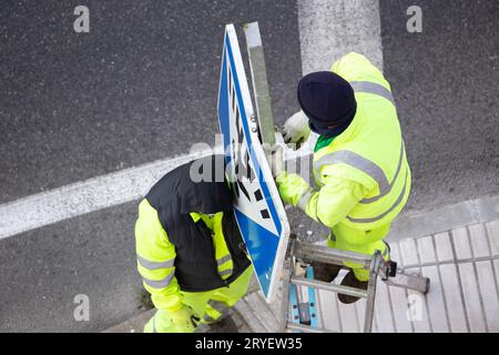 Workers changing a damaged road sign on street sidewalk Stock Photo