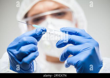 Female UK doctor or scientist wearing protective gear holding vaccine syringe with needle Stock Photo