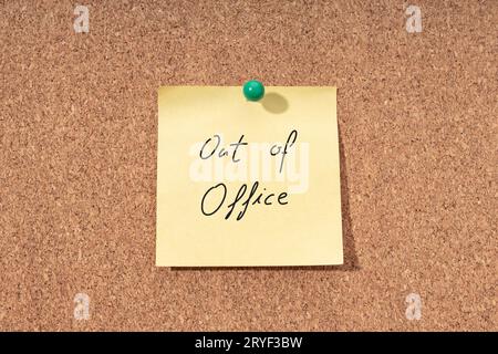 Yellow note with phrase out of office on cork board Stock Photo
