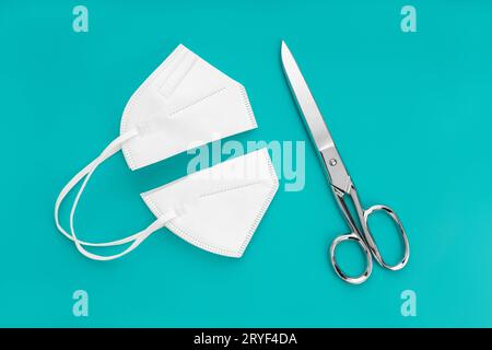 Face maskcut in half and scissors isolated on blue background. Concept of no longer be required to wear face masks Stock Photo