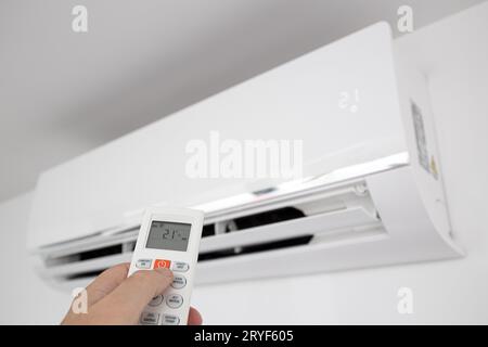 Hand operating a Remote control of a Domestic Air conditioner unit mounted on wall Stock Photo