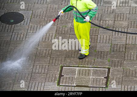 Worker holding a hose cleaning a sidewalk with water. Urban Maintenance or cleaning concept Stock Photo