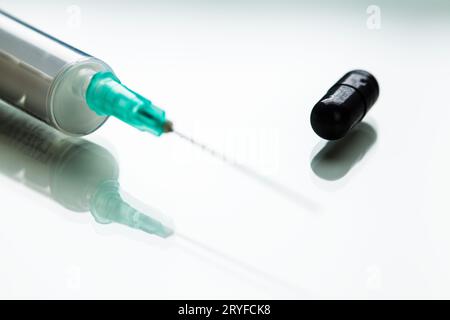 Green needle in syringe and black pill medication on white reflective surface Stock Photo