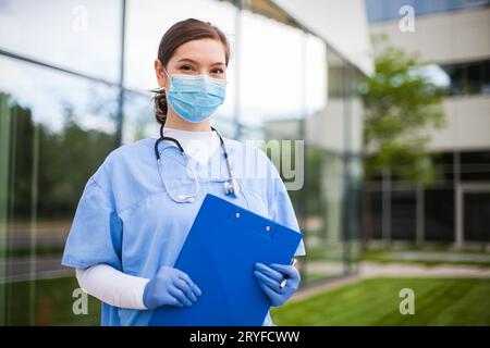 Portrait of beautiful young female doctor wearing blue protective uniform,standing outside the hospi Stock Photo