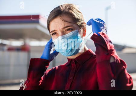 Young woman putting protective surgical face mask on Stock Photo