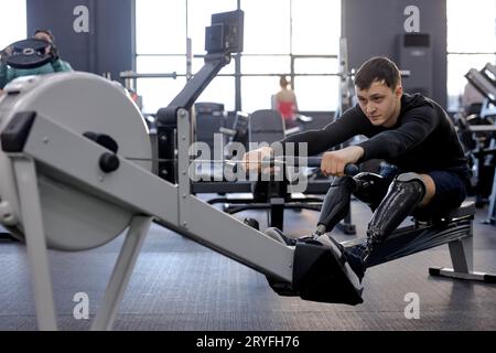 sportsman focuses on working out with stationary cardiovascular exercise machine, full length side view shot Stock Photo