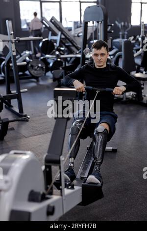 tired sweaty man training with rowing machine at gym, full length shot. motivation, endurance, willpower Stock Photo