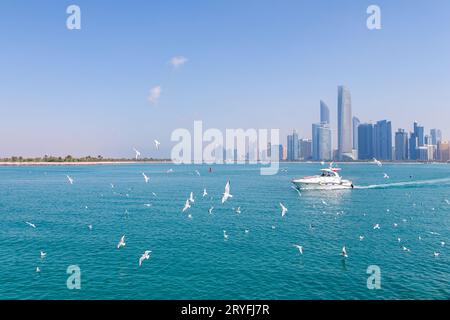 Abu Dhabi, UAE - February 16, 2022: Abu Dhabi cityscape during sunny day with seagulls flying around and travel boat in the wate Stock Photo