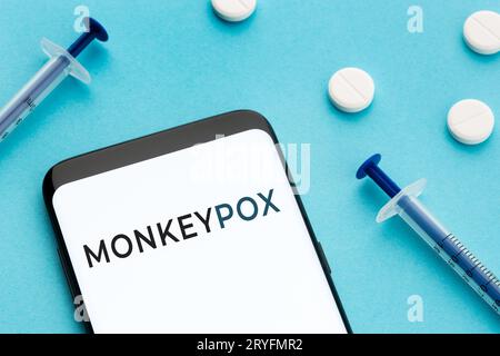 Samrtphone with text Monkeypox pills and syringes on blue background Stock Photo