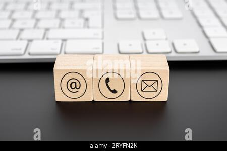Contact us icons on wooden blocks and computer keyboard on black desk Stock Photo
