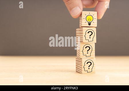 Creative idea and innovation concept. hand picking a wooden block with light bulb icon and human head with question mark inside. Stock Photo
