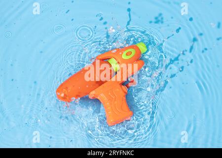Water gun toy splashing on blue water surface. Fun, leisure summertime background Stock Photo