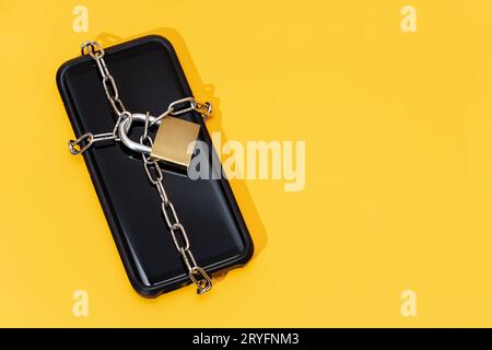 Phone security concept. Smartphone locked with chain and padlock on yellow background. Mobile security and data privacy Stock Photo