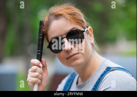 Blind red-haired woman sitting outdoors leaning on a cane.  Stock Photo