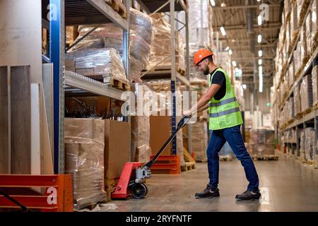 Young male warehouse worker carrying delivery to production stock using forklift. male staff in vest and orange helmet in place of work. Forklift driv Stock Photo