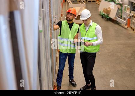 Focused men warehouse workers in working clothes uniforms talking together in warehouse, caucasian men counting goods in shelves, controlling the disc Stock Photo