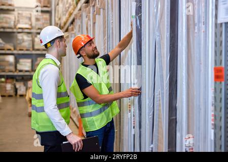 Focused male warehouse workers in working clothes talking together in warehouse, caucasian men counting goods in shelves, controlling the disctributio Stock Photo