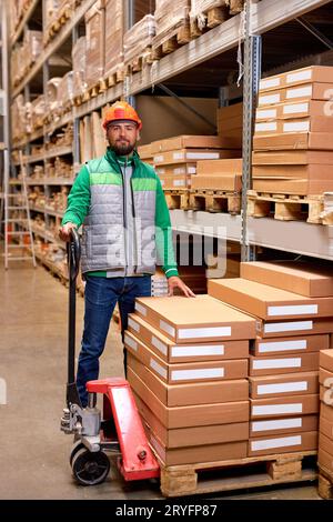 caucasian warehouse worker with manual pallet jack, working in storage room, transporting cardboard goods, boxes delivery. logistics and distribution Stock Photo