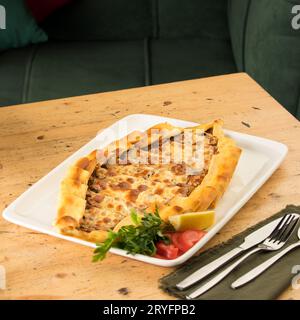 Traditional Turkish baked pide in a white plate on a wooden table Stock Photo