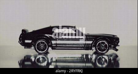 A macro photograph of black and white toy 1970s American muscle car reflecting on the road, with a dot-textured overlay. Stock Photo