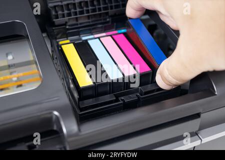 Human hand changing a blue ink cartridge of a multicolor inkjet printer Stock Photo