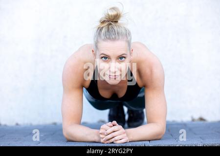 Attractive sporty woman concentrating in gym while doing fitness exercises. Young perfect shaped blonde doing plank Stock Photo