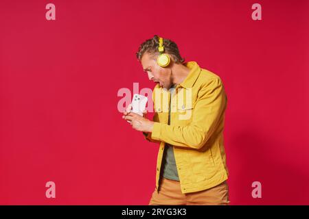 Joyful man sing while recording his voice using smartphone. Singing handsome man enjoying his favorite song using phone and wire Stock Photo