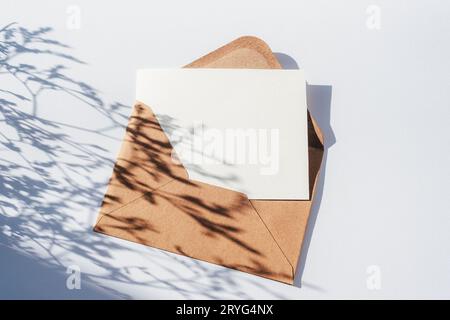 Envelope with blank card and flowers shadow on light blue background. Top view, flat lay, mockup. Stock Photo