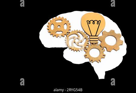 White human brain shape with wooden gears and light bulb inside isolated on black background. Creative education and enlightenment related concept. Stock Photo