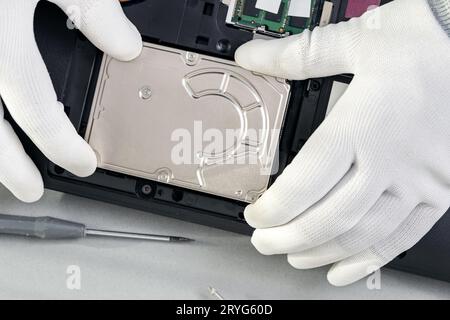 Technician hands removing an old mechanical hard disk from a laptop. Top view Stock Photo