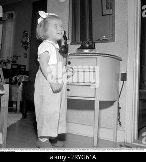 In the 1950s. A little girl is playing with a telephone, holding the handset, reciever against her ear to listen. Sweden 1950. Conard ref 1526 Stock Photo