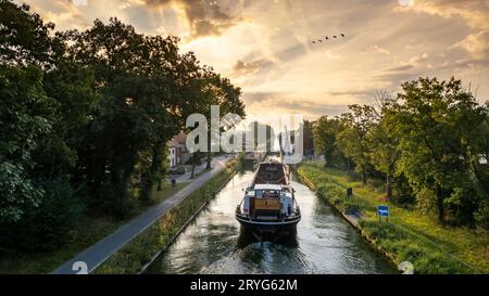 Aerial view of a colourful dramatic sunrise sky over a canal with a cargo boat in Belgium. Canals with water for transport, agri Stock Photo