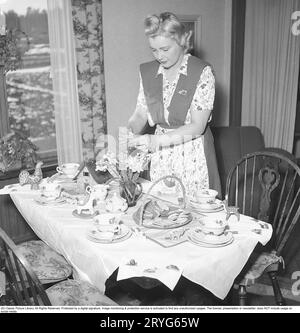 In the 1940s. A woman has set a table for Easter and arranges daffodils to be placed in a vase on the table. The table is set with fine china with double plates. A cake plate with sponge cake and cookies is on the table. An Easter bun is placed on the table. Sweden 1945. Kristoffersson ref N72-5 Stock Photo