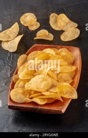 Potato chips or crisps in a wooden bowl on black Stock Photo