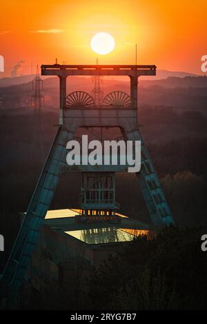 Vertical shot of a headframe tower with a golden sun setting in the background in Herten, Germany Stock Photo
