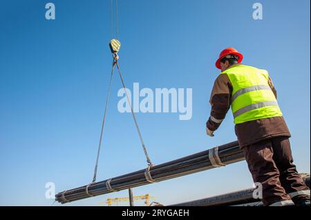 A low-angle shot of a person standing trying to carry industrial pipes on a crane Stock Photo