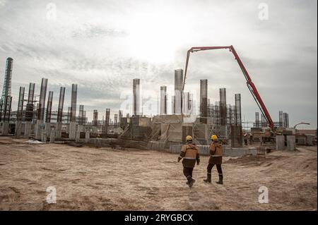 Two workers in special equipment and yellow helmets with factory construction in the background Stock Photo
