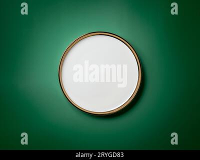 Empty white round plate with golden border on deep green background Stock Photo