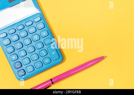 Flat lay of Calculator and pen on yellow background. Vibrant colors Copy space Stock Photo